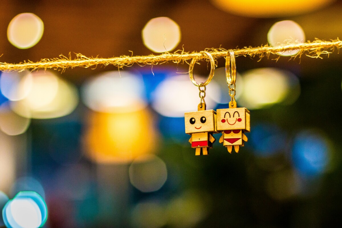 Charming wooden cartoon keychain dolls hanging with vibrant bokeh lights in the background, creating a playful and colorful ambiance.